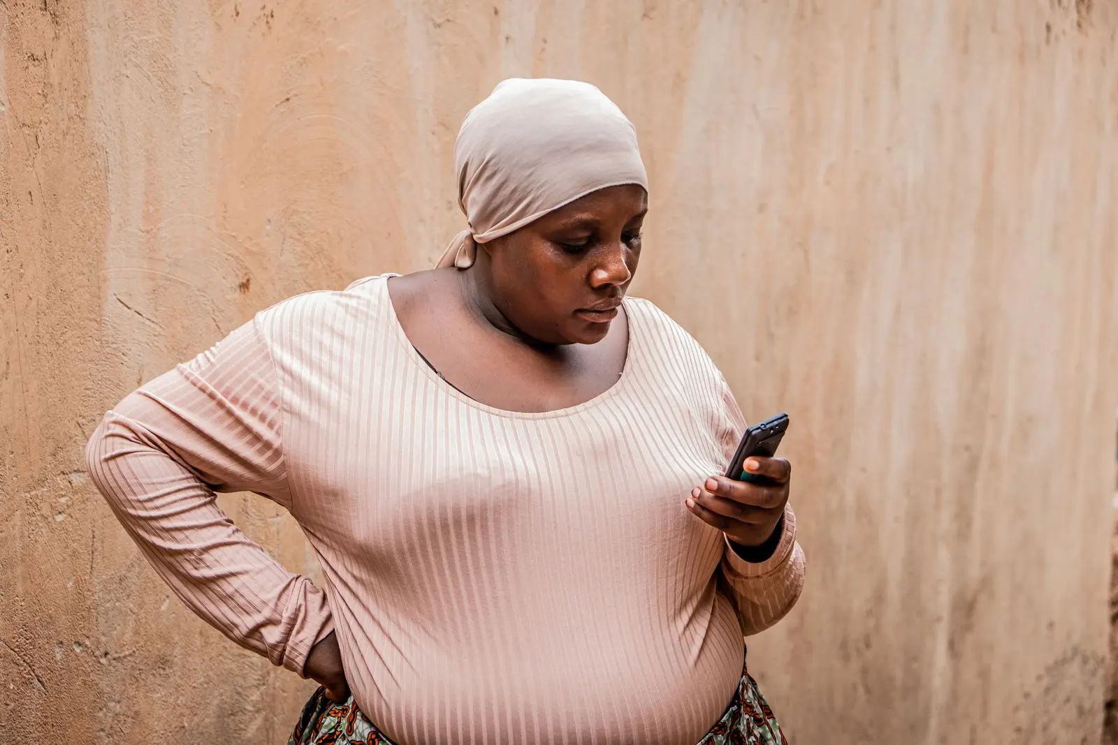 Femme consultant son smartphone contre un mur extérieur — photo d’illustration (banque d’images)