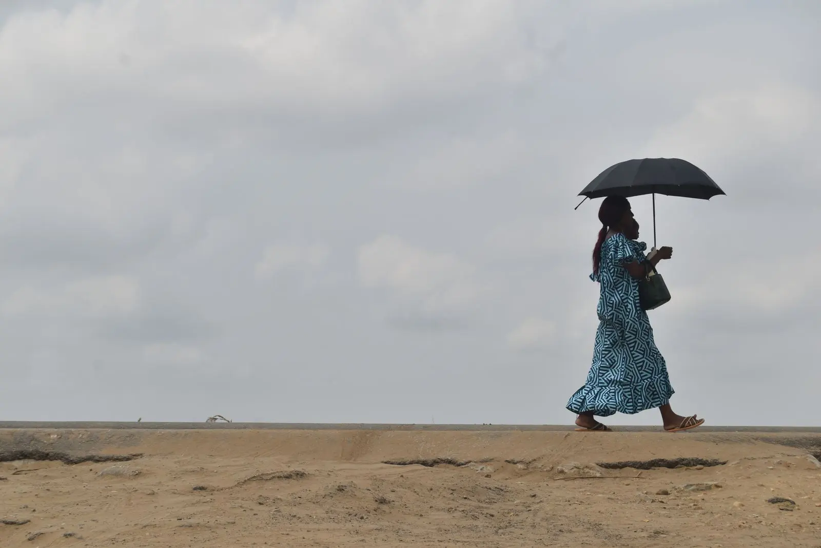 Une femme marche avec un parapluie sous un ciel nuageux — photo d’illustration (banque d’images)