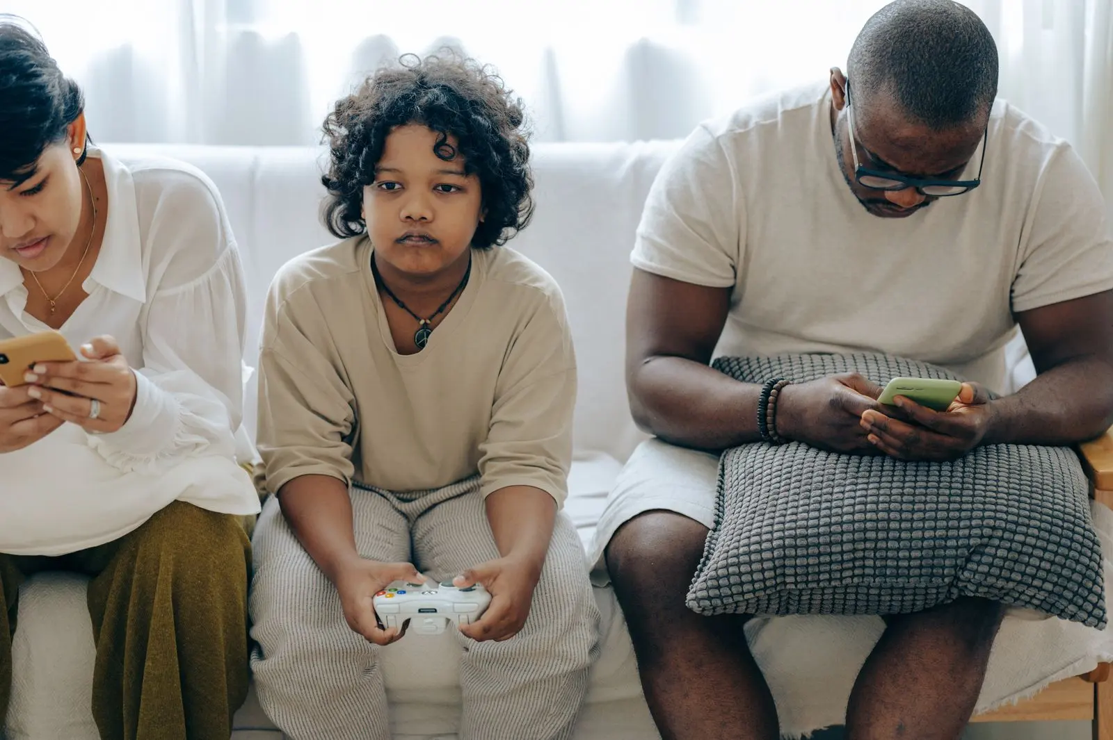 Enfant jouant à la console entre deux parents connectés — photo d’illustration (banque d’images)
